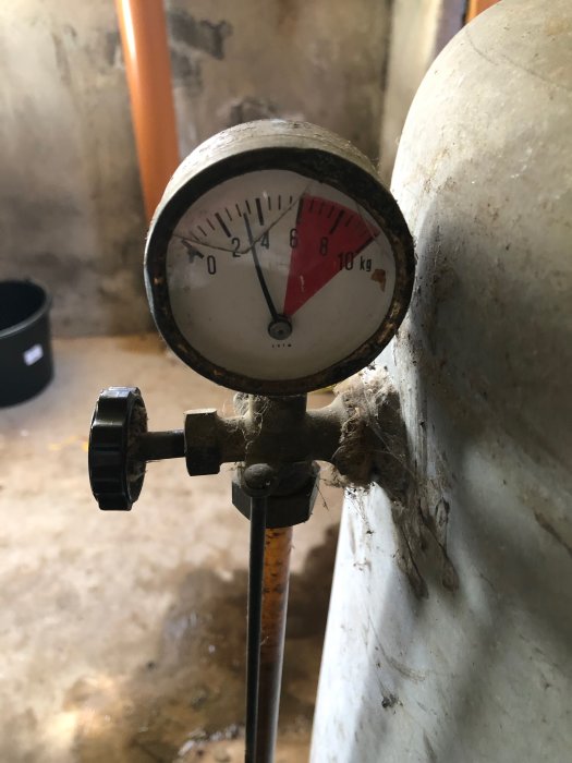 Manometer med lågt tryck i en teknisk installation, omgiven av otydlig utrustning och en betongvägg.