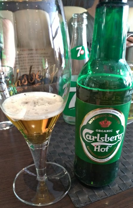 Ett glas med pilsner och en gröna Carlsberg Hof-ölflaska på restaurangbord med en 7up-flaska i bakgrunden.