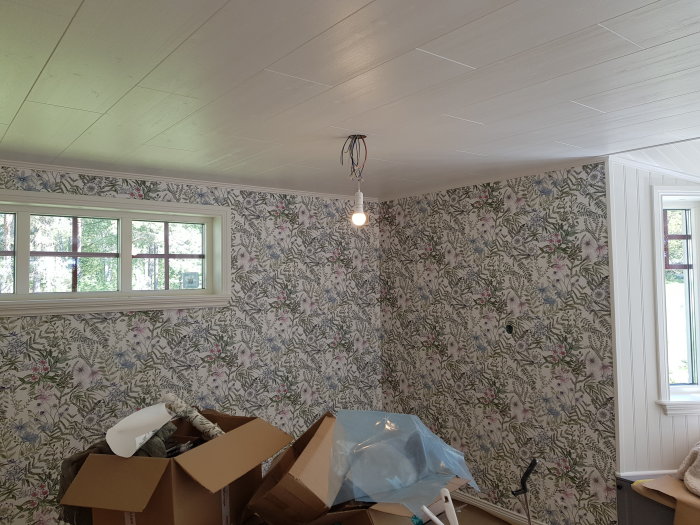 Renoverat rum med blommiga tapeter på väggarna och renoveringsmaterial på golvet.