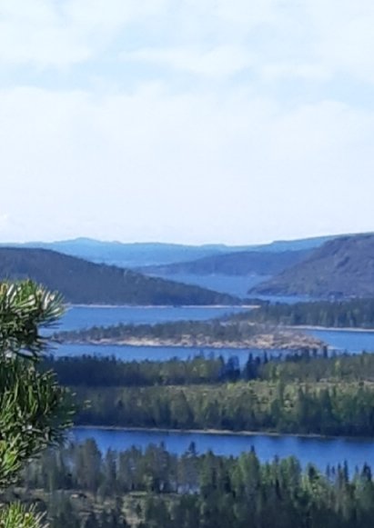Vy över skogklädda kullar och en slingrande flod eller sjö med blått vatten under en molnig himmel.