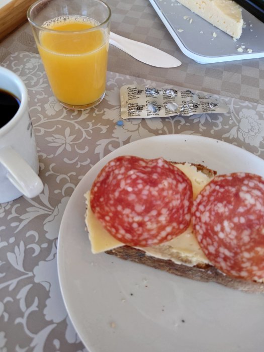 Frukost med macka med salami och ost, apelsinjuice och kaffe vid ett köksbord.