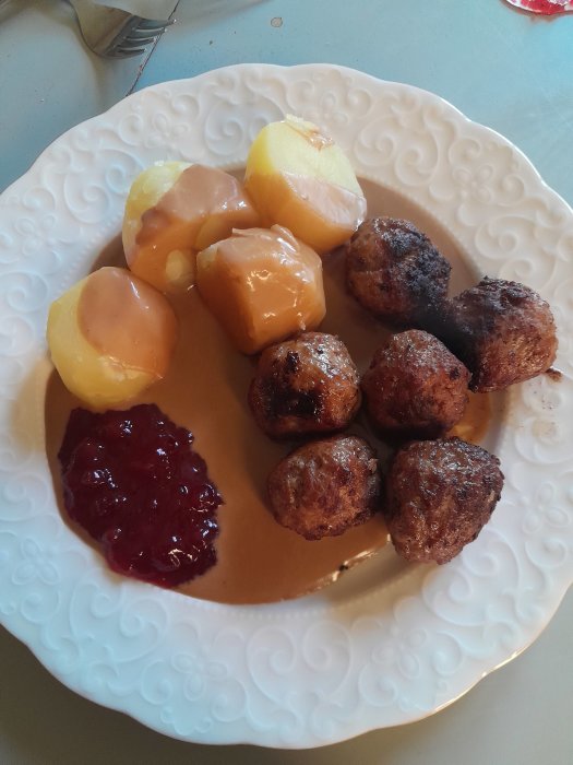 Svenska köttbullar med potatis, brunsås och lingonsylt på en vit tallrik.