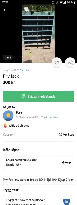 Blått prylfack med många fack i metall till salu för 300 kronor, utomhus på en trottoar.