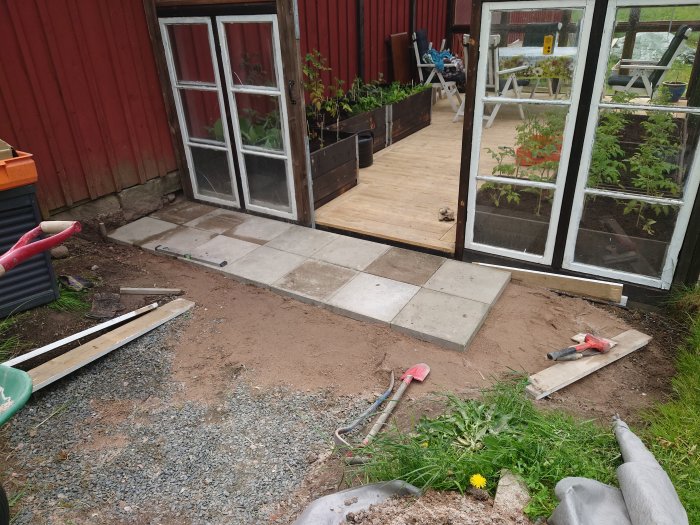 Anläggning av sluttande plattgång med 40x40 plattor framför ett växthus.