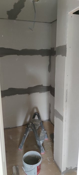 Renoveringsarbete i badrum, väggar med spackel och gips, samt en stege och hink på golvet.