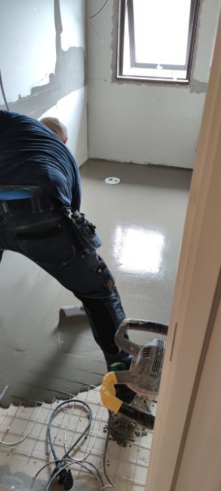 Arbetare häller flytspackel på badrumsgolv vid installation av toalett.