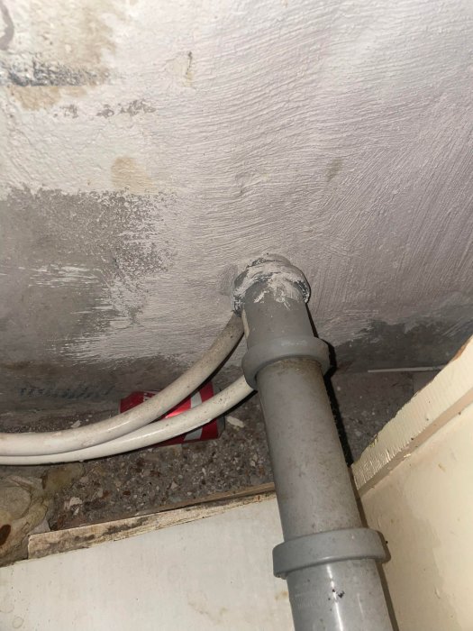 VVS-installation med ett grått avloppsrör genom en vägg och kablar intill.