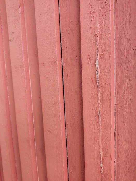 Glipa mellan rödmålade träpaneler på en fasad, med behov av fogning.