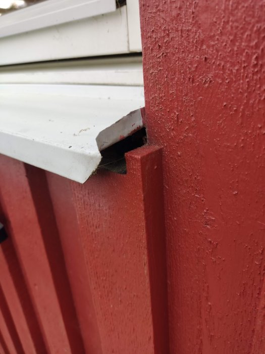 Stort hål vid sidan av ett vitt fönsterbleck mot en röd träfasad.
