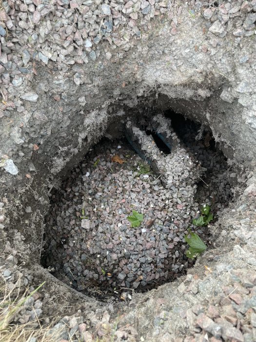 Slukhål i gräsmatta med synligt grus och delar av ett svart rör som antyder koppling till bergvärmesystem.