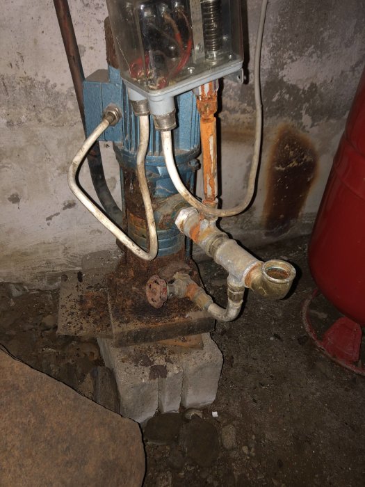 Gammal rostig pump monterad på betongblock i ett smutsigt utrymme, använd för bevattning.