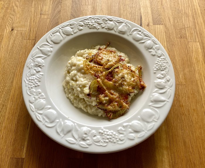 En tallrik med vit och krämig citronrisotto toppad med gyldenbrunt getostbakad fänkål på ett träbord.