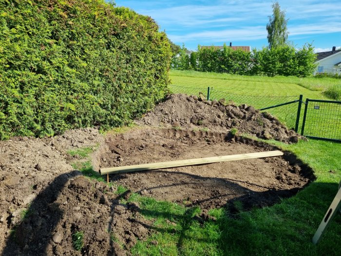 Utgrävd ojämn grop i trädgård förberedd för ovanmarkpool med en träplanka för att kontrollera planheten.