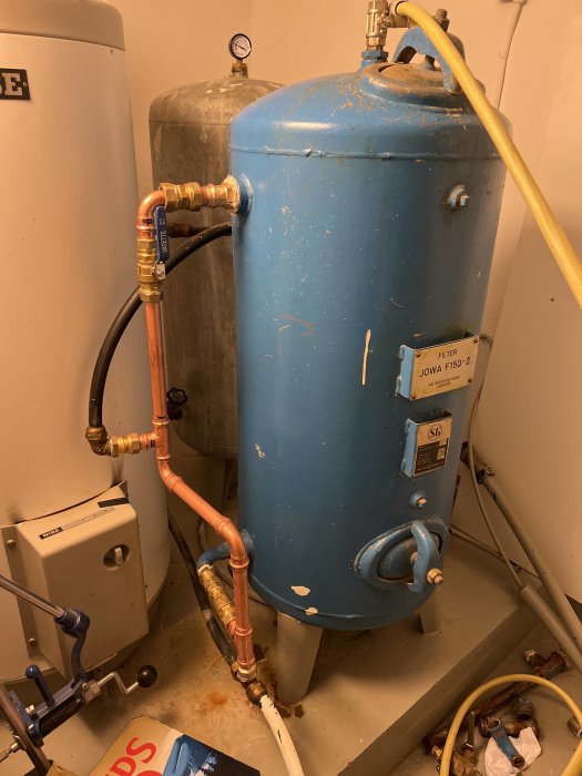 Äldre blå vattenfilter med inkommande svart rör och utgående vitt rör, kopplat till kopparrör, fråga om rätt inkoppling.