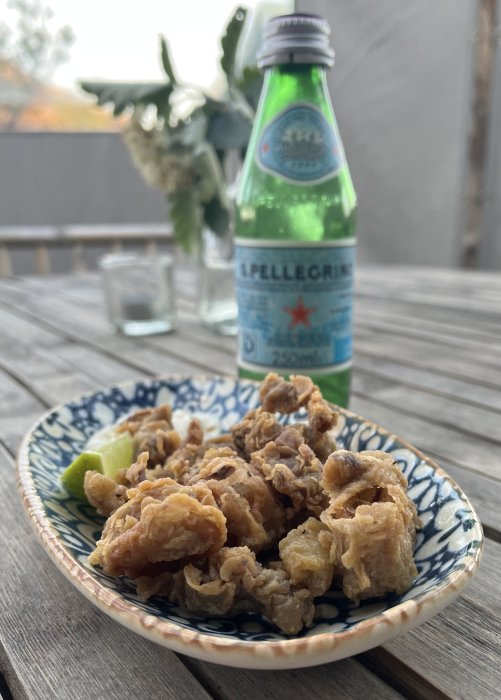 Friterade calamares på mönstrad tallrik med limeskiva och Pellegrino-vattenflaska i bakgrunden.