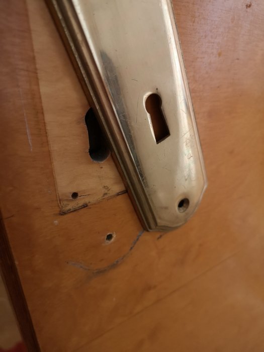 Träskruvhål och skrapmärken på trädoor bredvid en monterad låsskylt.