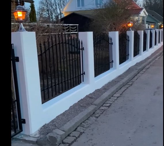 Vitmurade pelare med svart smidesstaket längs en gatstenbelagd trottoar.