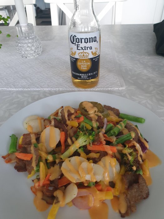 Måltid med wokgrönsaker, kyckling, kebab, jalapenos och mayo, flankerad av en Corona öl.