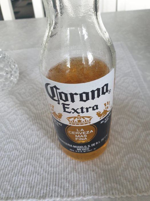 En öppnad flaska Corona Extra öl på ett vitt borddu.