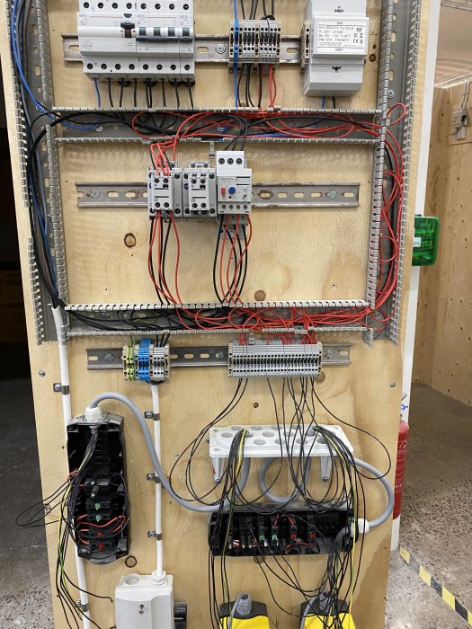 Elkraftteknik-uppgift med kretsschema för start/stopp och nödstopp av elmotor på träpanel.