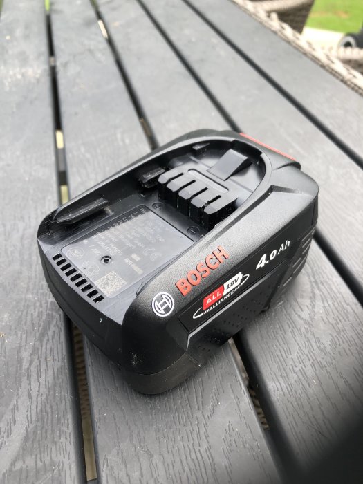 Bosch 18V 4.0Ah batteri liggandes på en mörk träbänk.