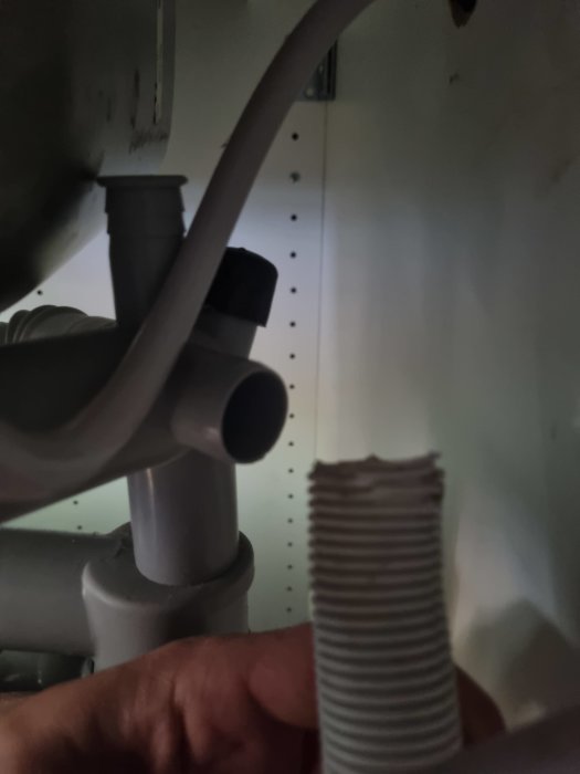Hand som håller flexibel avloppsslang nära PVC-vattenlås under en diskbänk.