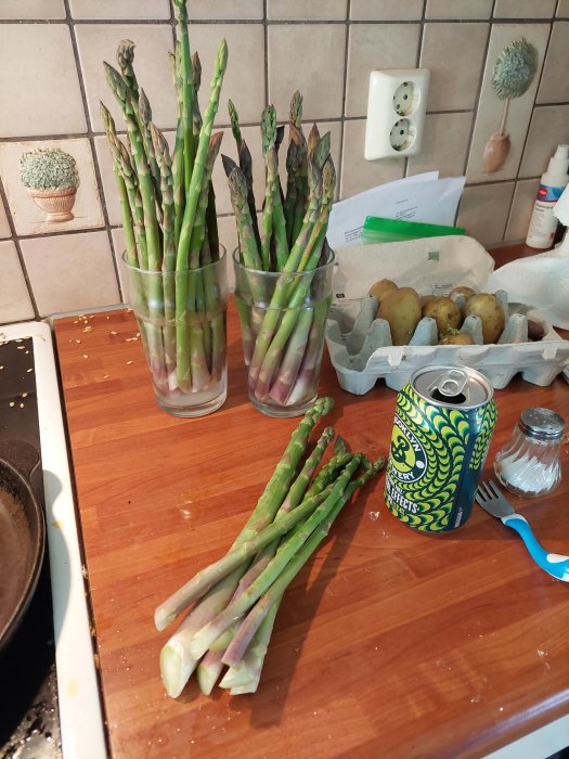 Färsk skörd av grön sparris i glas och på skärbräda på köksbänk.