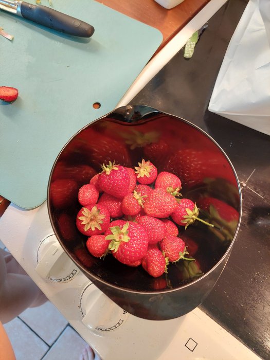 Skål med ny-skördade färska jordgubbar på ett köksbord med en skalkniv.