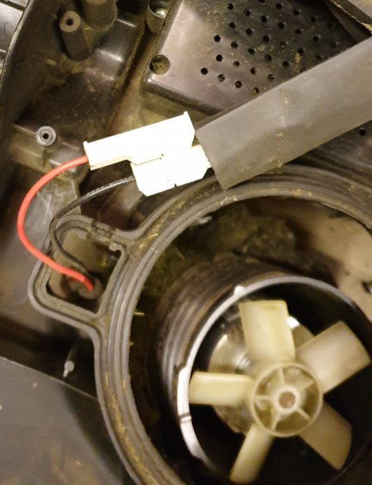 Öppen mekanisk enhet med synlig fläkt och smutsiga komponenter, tejpade elektriska kablar syns också.