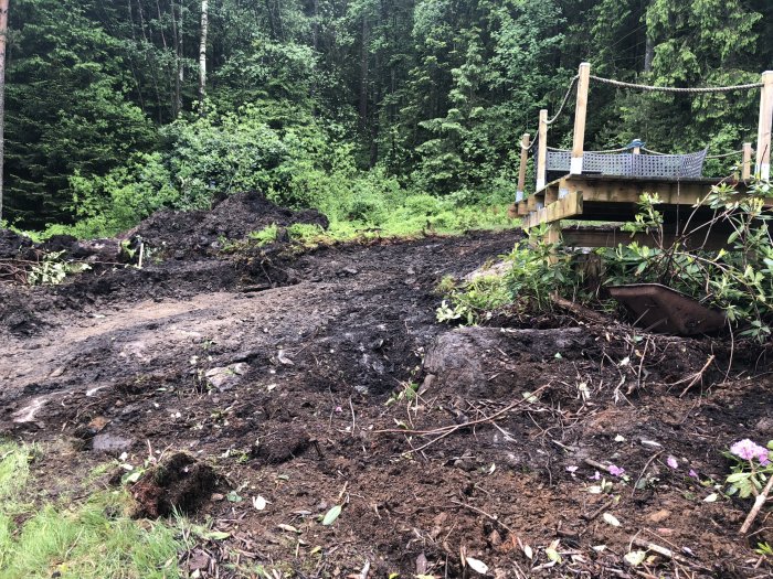 Grävmaskinsarbete på en blivande byggtomt med uppschaktad jord och en del av en trädgårdslekplats synlig.