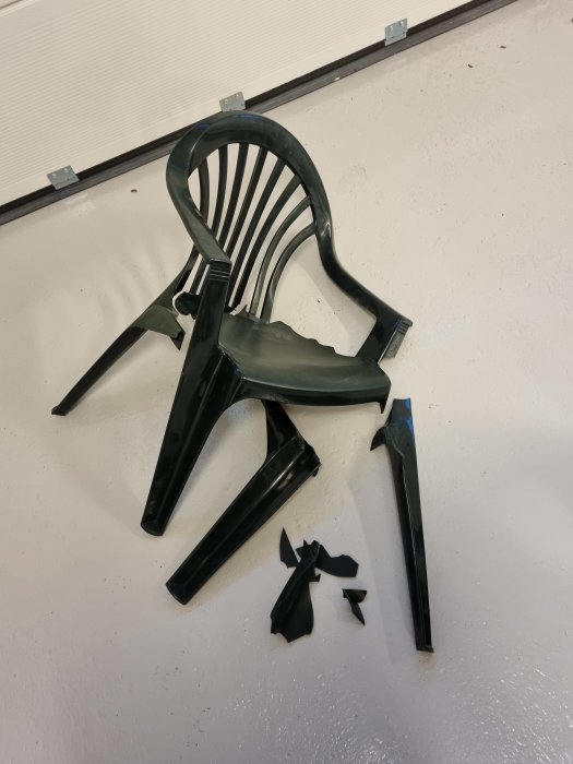 Söndrig svart plaststol med brutna ben och delar utspridda på ett golv.
