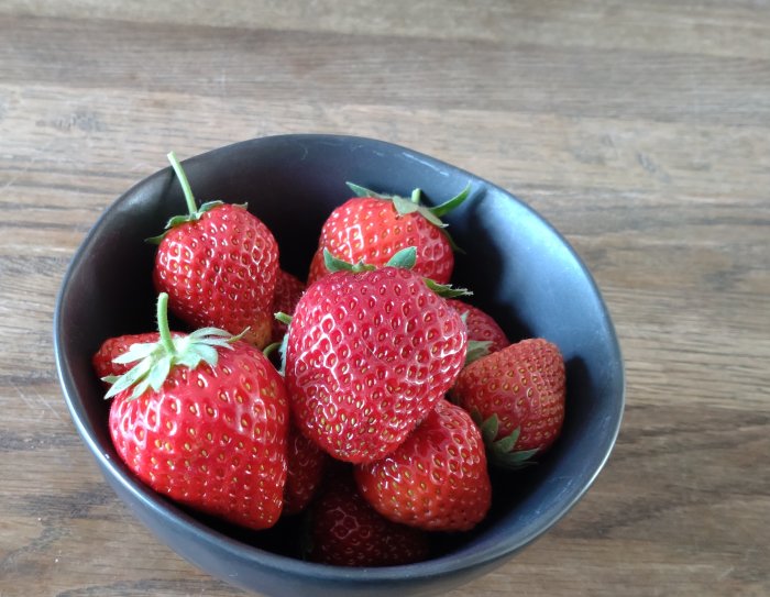 Mogna jordgubbar i en svart skål på ett träbord.