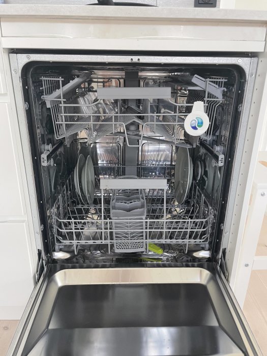Öppen diskmaskin under köksbänk med synlig inredning och diskmedelsbehållare.