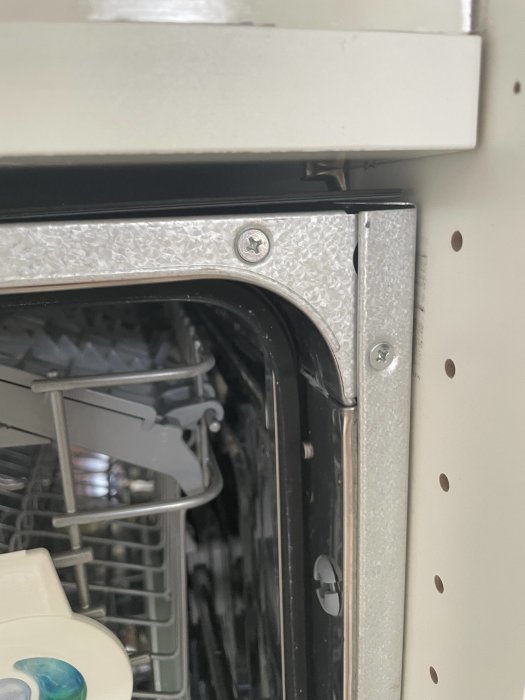 Diskmaskin installerad under köksbänk med synlig kant och skruv vid luckan, bänken syns ovanför.