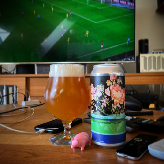 Ölglas fyllt med öl och burk framför fotbollsmatch på TV-skärm.
