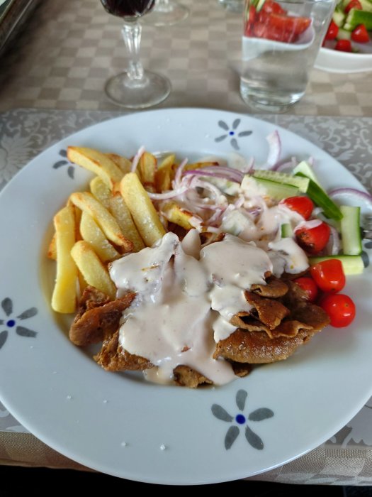 Hemgjord kebabtallrik med noga skurna grönsaker, pommes och vitlökssås på ett blommönstrat fat.