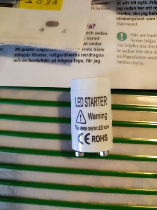 En glimtändare för LED-rör märkt med varningsinformation och CE-ROHS-symboler framför ett lysrör.