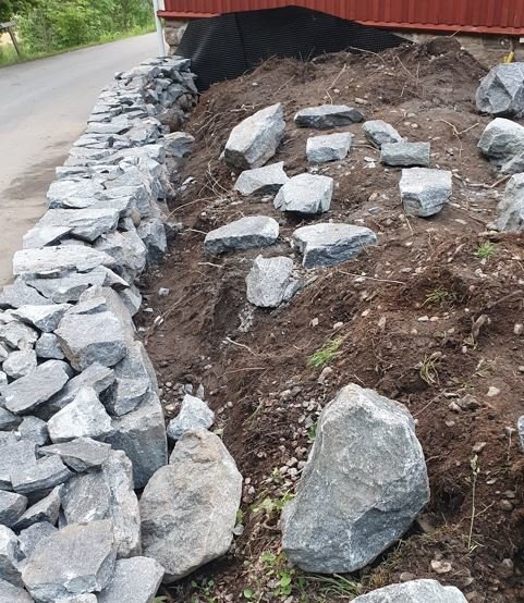 Nybyggd stenmur längs en grusväg med jord och utspridda stenar bakom muren.