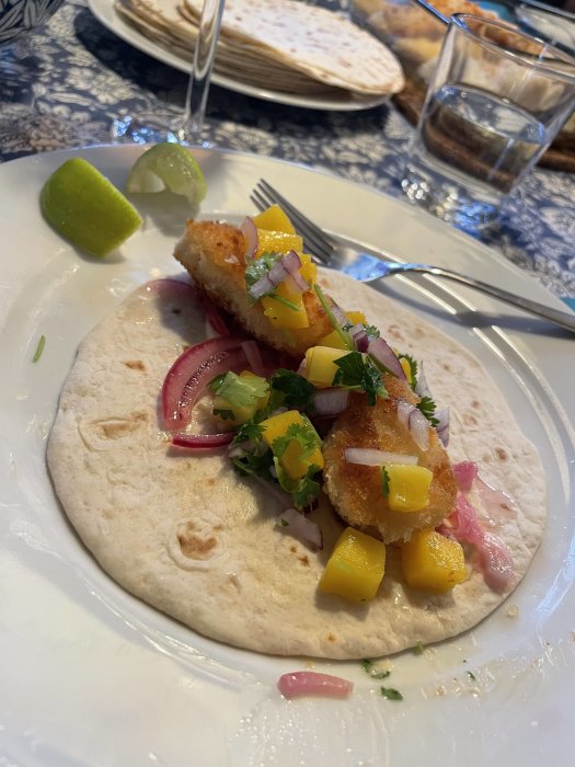 Fish taco med mangosalsa och picklad rödlök på en tortilla, serveras med lime.