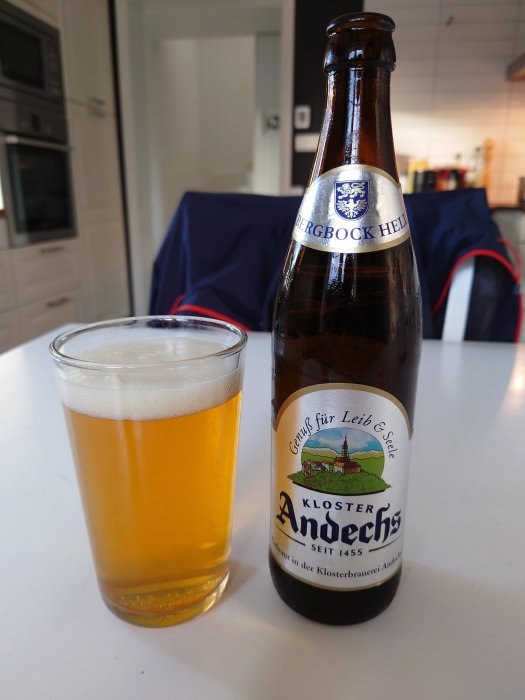 En ölflaska märkt "Kloster Andechs" bredvid ett glas med öl på ett köksbord.