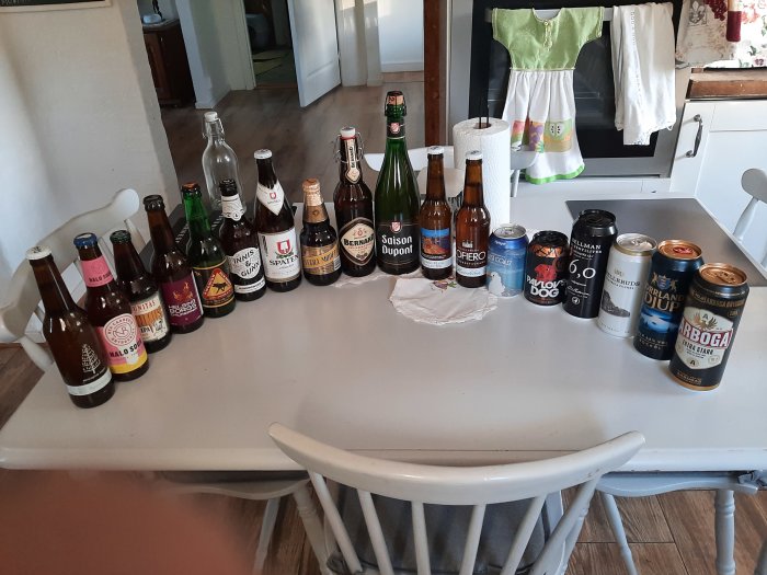 Ölflaskor och burkar uppradade på ett köksbord, en blandning av olika ölsorter och varumärken.