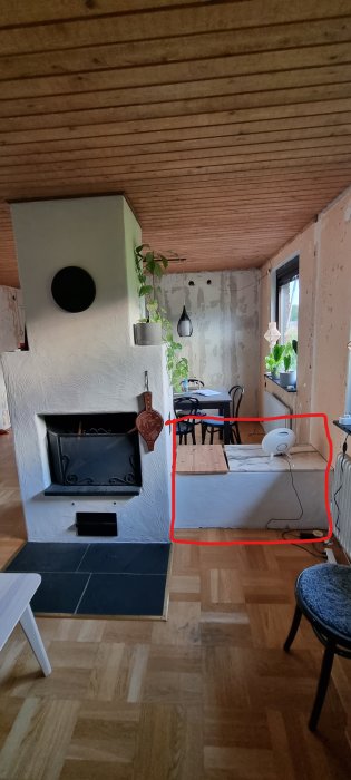 Vardagsrum med öppen spis, röd markering visar del som önskas borttagen, vedförvaring synlig.