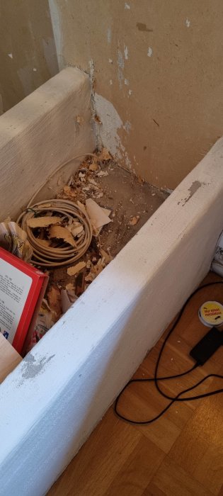 Hörn av vardagsrum med öppen spis och markerad del för avlägsnande, vedförvaring synlig.
