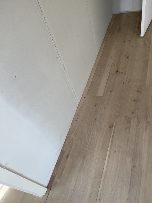 Hörn av ett rum i pågående renovering med nyinstallerat laminatgolv och obehandlad gipsvägg.