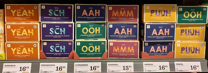 Hyllor fyllda med färgglada te-förpackningar märkta med uttryck som "YEAH", "SCH", och "AAH".