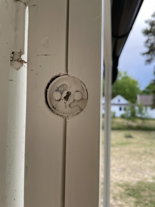 Närbild på en sliten fönsterskruv på ett vitt fönster med en suddig bakgrund.