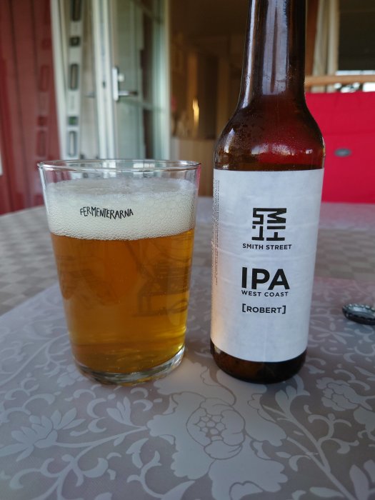 Ett glas med IPA-öl vid sidan av en ölflaska märkt "Smith Street IPA", på ett bord utomhus.