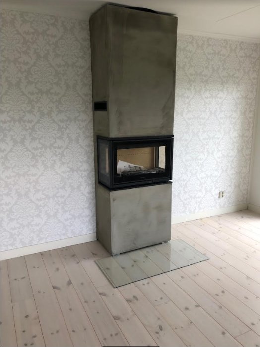 Contura i8 kamin installerad i hörn med tapetserade väggar och trägolv.