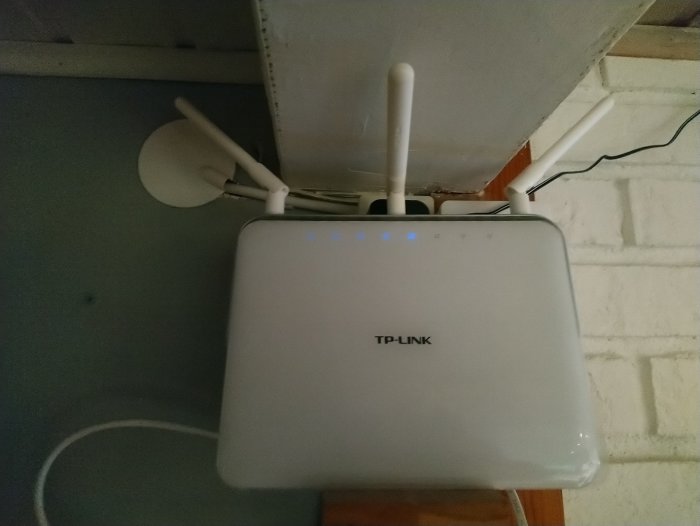 TP-Link router upphängd på en vägg med tre antenner och lysande blå indikatorlampor.