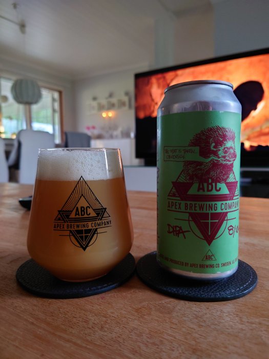 Ölglas med märket Apex Brewing Company och en burk öl från samma märke framför en TV.